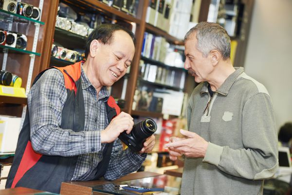 دستیار فروشنده با نمایش دوربین عکاسی دیجیتال در فروشگاه به خریدار کمک می کند