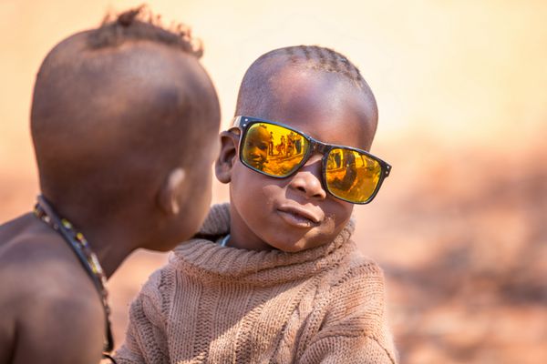 EPUPA نامیبیا - 4 آگوست یک کودک ناشناس هیمبا با عینک آفتابی در حالی که گردشگران از سکونتگاه در 4 اوت 2013 در نامیبیا بازدید می کنند عکس می گیرد