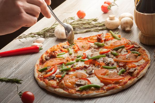 پیتزا با گوشت ژامبون سبزیجات سرآشپز روغن زیتون را از قاشق می ریزد در پس زمینه شراب قرمز روغن زیتون گوجه فرنگی گیلاس قارچ و گیاهان