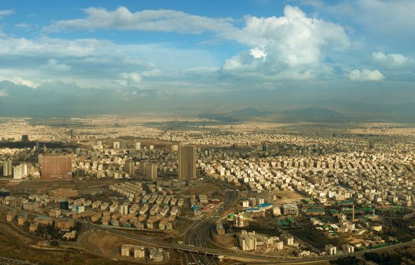 تصویر هوایی از شهر تهران در برابر آسمان آبی با ابرهای سفید کرکی بر فراز برج میلاد