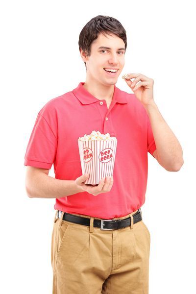 مرد جوان خندان در حال خوردن ذرت بو داده جدا شده در پس زمینه سفید