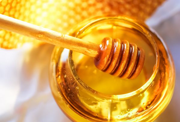 دیپر عسل روی زمینه لانه زنبور عسل نکته عسلی در ظرف شیشه ای و موم لانه زنبوری