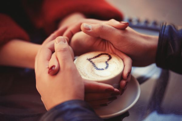 چهار دست دور یک فنجان قهوه با نقاشی قلب پیچیده شده است