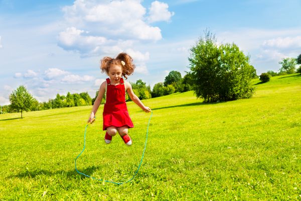 دختر بچه 6 ساله زیبا که در روز آفتابی تابستان از روی طناب در پارک می پرد