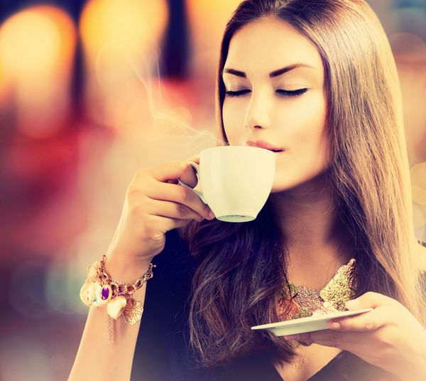 قهوه دختر زیبا در حال نوشیدن چای یا قهوه در کافه زن مدل زیبا با فنجان نوشیدنی داغ رنگ های گرم تنیده