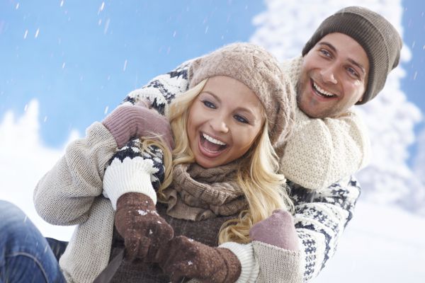 زوج عاشق خوشبختی که در زمستان در فضای باز سورتمه می‌کشند و می‌خندند