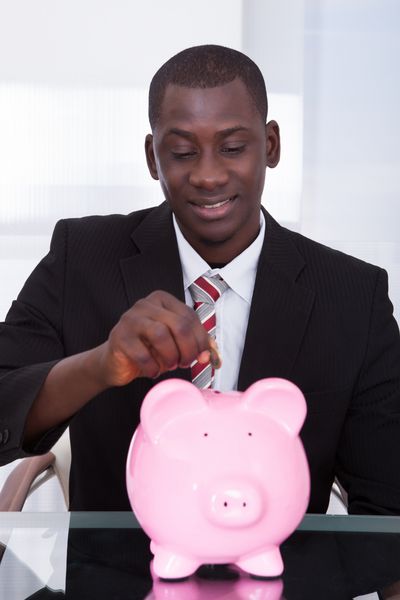 پرتره یک تاجر جوان آفریقایی در حال فرو کردن سکه در Piggybank