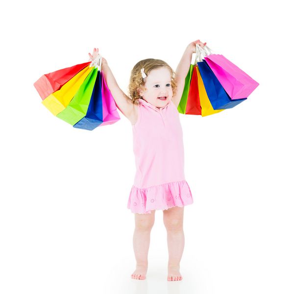 دختر کوچولوی شایان ستایش با موهای مجعد که لباس صورتی پوشیده است پس از فروش و خرید پیشنهاد ویژه خوشحال است که کیف های رنگارنگ خود را نشان می دهد