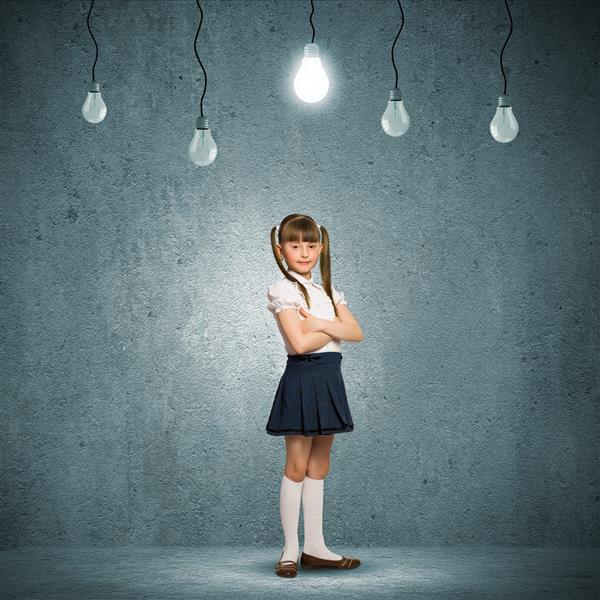 دختر مدرسه ای ناز مقابل دیوار خاکستری با لامپ های آویزان در بالا