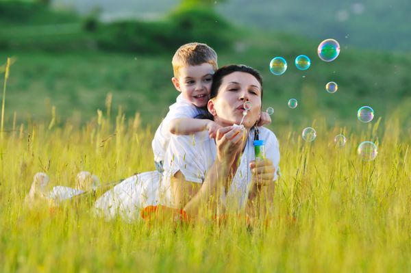 کودک و زن شاد در فضای باز با حباب صابون در چمنزار بازی می کنند