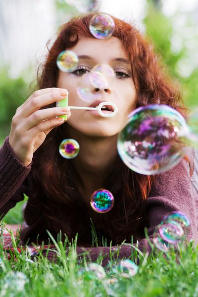 زن جوان در حال دمیدن حباب در طبیعت