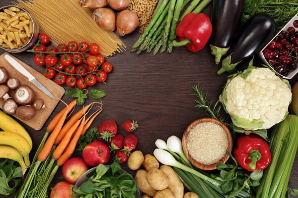 عکس روی میز پر از سبزیجات تازه میوه و سایر غذاهای سالم با فاصله ای در وسط برای متن