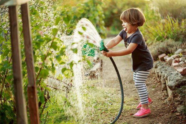 دختر کوچولوی شاد در حال آبیاری باغ