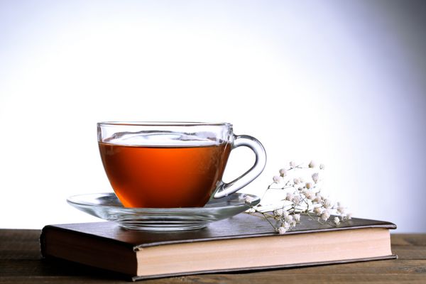 فنجان چای داغ روی کتاب با گل روی میز در زمینه خاکستری