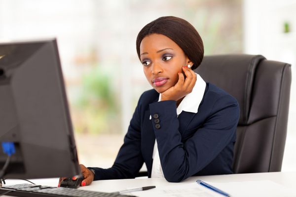 زن تاجر آفریقایی آمریکایی متفکر که در دفتر به صفحه کامپیوتر نگاه می کند