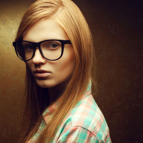 پرتره جوانی با موهای قرمز زیبا که عینک های شیک و پیراهن معمولی به چشم دارد و روی پس زمینه طلایی ژست گرفته است نزدیک فضای کپی شات استودیویی