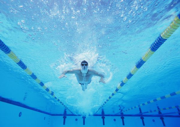 عکس زیر آب از شناگر مرد در حال شنا در استخر