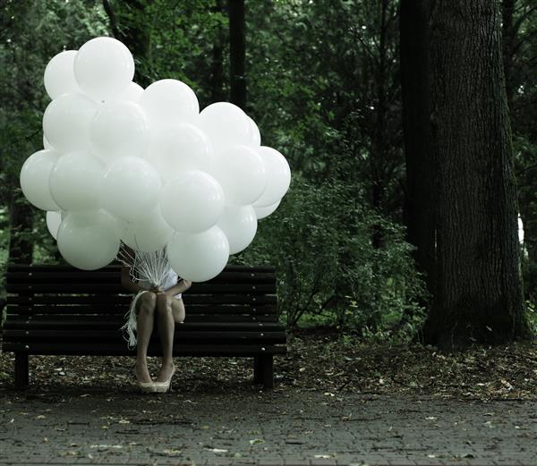احساساتی بودن نوستالژی زن تنها با بالن های هوا روی نیمکتی در پارک نشسته است