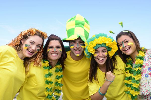گروهی از هواداران شاد فوتبال برزیل در حالی که پرچم برزیل در هوا در حال اهتزاز است پیروزی را جشن می گیرند