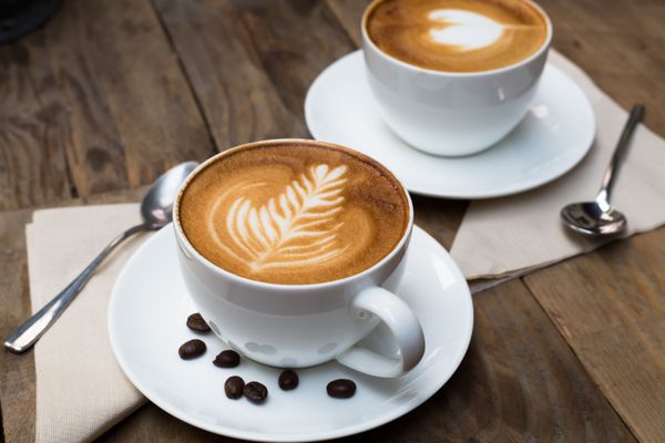 فنجان قهوه لاته آرت داغ روی میز چوبی