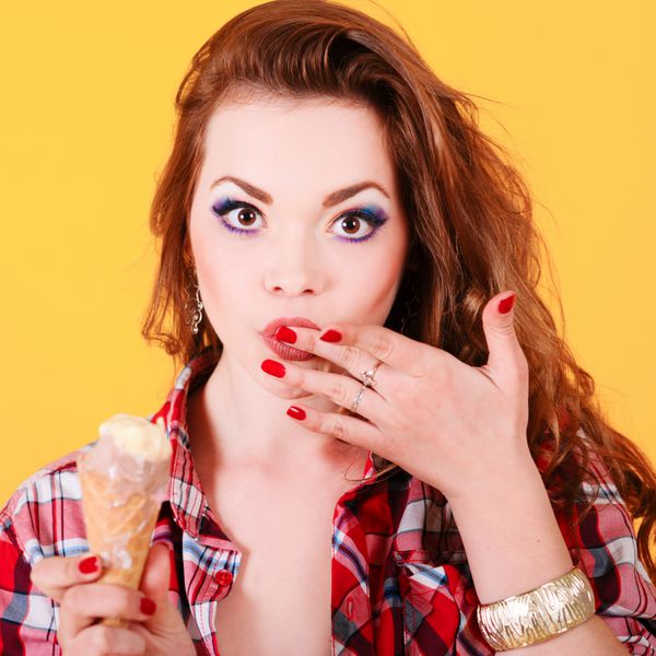 زن جوان در حال خوردن بستنی در زمینه زرد