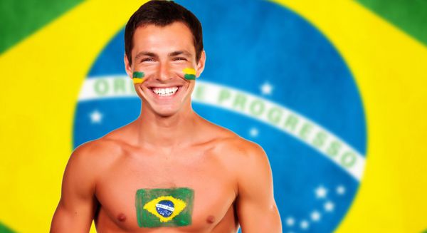 طرفدار برزیلی خوشحال که بالای پس زمینه پرچم برزیل ایستاده است