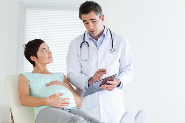 دکتر در حال توضیح دادن چیزی برای یک زن باردار در اتاق
