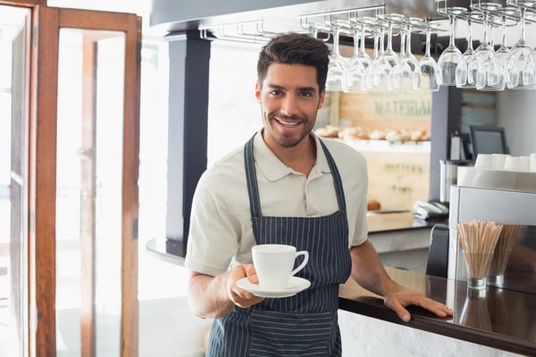پیشخدمت جوانی که در کافه لبخند می زند و فنجان قهوه در دست دارد