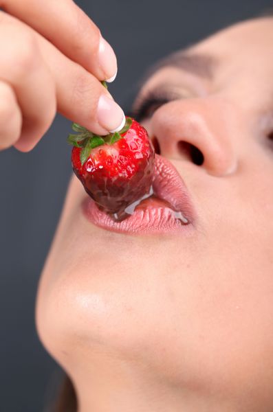 نمای نزدیک از زن در حال خوردن توت فرنگی در شکلات