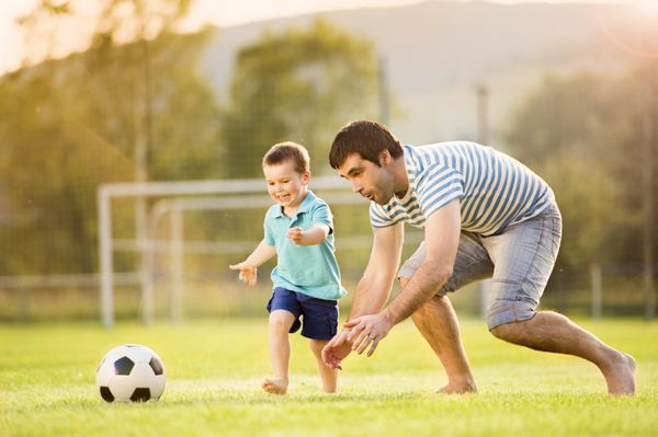 پدر جوان با پسر کوچکش در حال فوتبال در زمین فوتبال