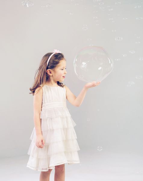دختر بچه دوست داشتنی خنده دار که با حباب های صابون بازی می کند