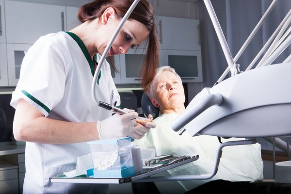 زن دندانپزشک در حال کار با یک بیمار مسن در کلینیک دندانپزشکی