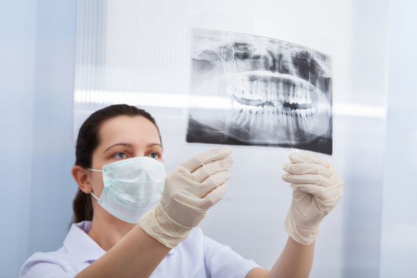 نمای عقب دندانپزشک زن که در کلینیک به اشعه ایکس دندان نگاه می کند