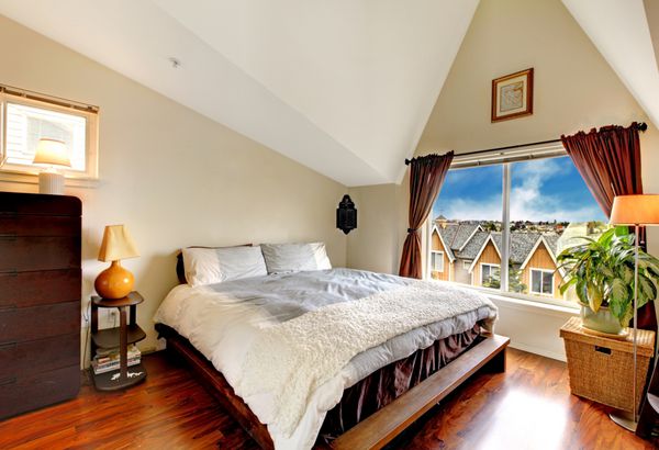 اتاق خواب زیبا با سقف طاقدار کف چوبی و پنجره مبله با تخت کمد و پاتختی اتاق با سبد حصیری و گیاه تزئین شده است