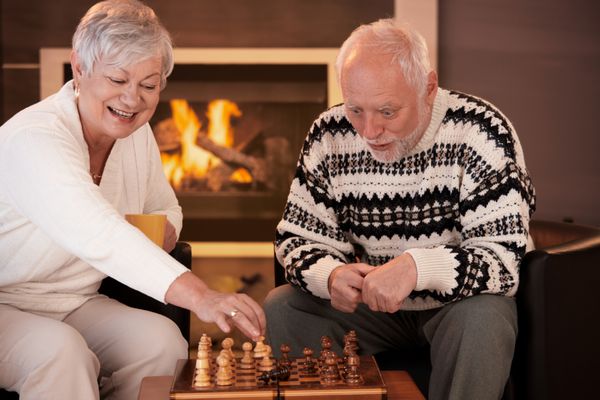 زوج سالخورده ای که در شب زمستان در خانه با شطرنج سرگرم می شوند زنی که مرد شطرنج را روی تخته حرکت می دهد مرد متعجب به نظر می رسد