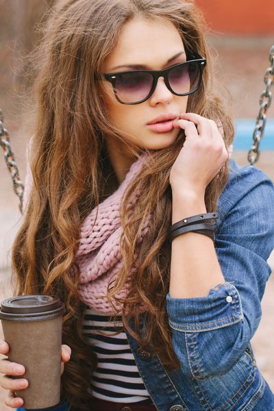 پرتره یک دختر سیاه و سفید زیبا با عینک آفتابی نوشیدنی را در یک دست دست دیگر را در کنار صورت خود نگه داشته است نشستن در پارک روز گرم آفتابی بیرون از خانه