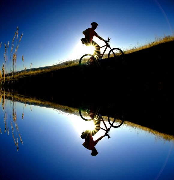 دوچرخه‌سواری در کوهستان تا مسیری در کوه‌ها انعکاس‌هایی را در آب نشان می‌دهد