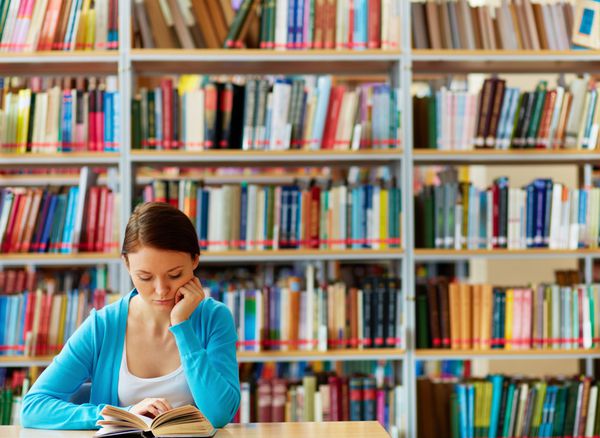 پرتره دانشجوی باهوش با کتاب باز در حال خواندن آن در کتابخانه کالج