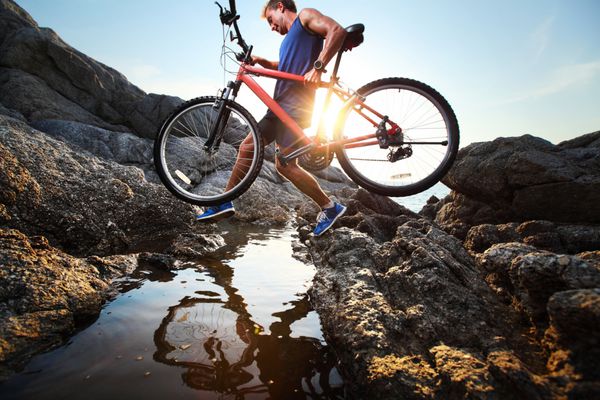 ورزشکار جوان در حال عبور از زمین های صخره ای با دوچرخه در دستانش
