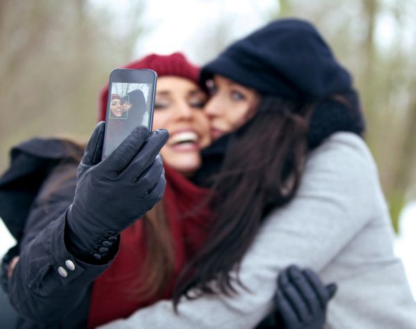 دو زن سرگرم کننده هنگام عکس گرفتن با تلفن هوشمند خوشحال به نظر می رسند