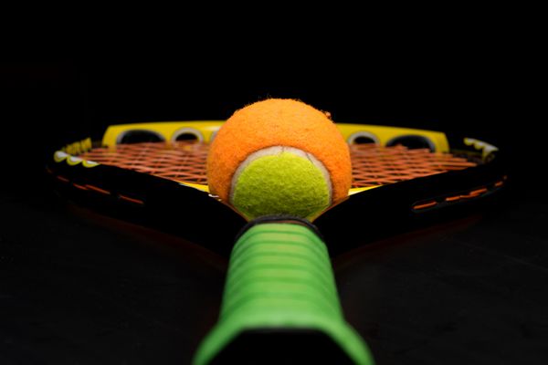 توپ تنیس برای بچه ها با راکت تنیس با دسته سبز و رشته های نارنجی روی زمینه مشکی