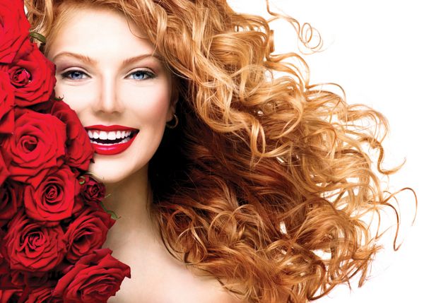 زن زیبایی با موهای مجعد قرمز بلند و مدل موی زیبای رز قرمز دختر مدل مد با دمیدن موهای موج دار سالم جدا شده در پس زمینه سفید پرتره خانم با دسته گل رز قرمز