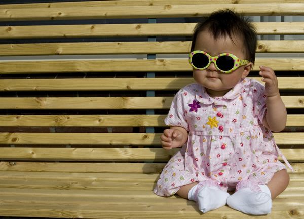 دختر بچه شیرینی که روی ایوان نشسته و عینک آفتابی زده است