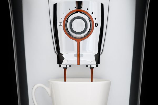 نمای نزدیک از دستگاه قهوه اسپرسو اتوماتیک مدرن فنجان سفید زیر نازل ریختن قهوه از دستگاه پس زمینه سیاه