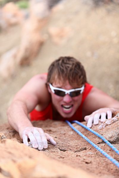 مردی در حال کوهنوردی کوهنورد مرد قوی در چالش دشوار در طول صخره نوردی با طناب روی دست در پیش زمینه تمرکز کنید