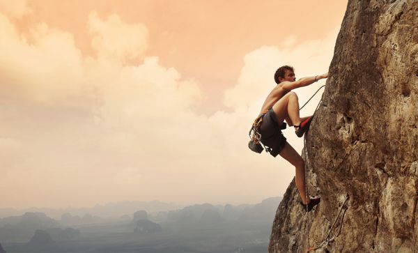 مرد جوانی در حال بالا رفتن از دیوار سنگ آهکی با دره وسیع در پس زمینه