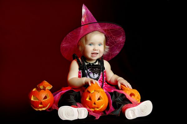 دختر کوچک در لباس جادوگر با کدو تنبل هالووین