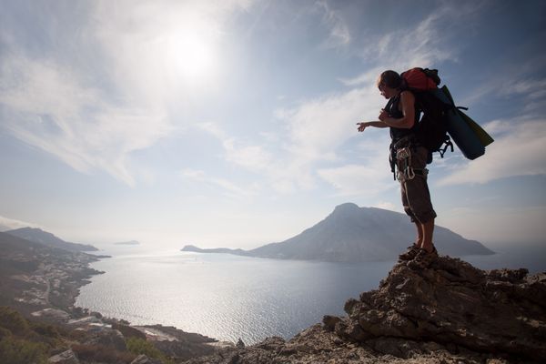 مرد جوانی که روی صخره ای در مقابل منظره زیبای دریا ایستاده است