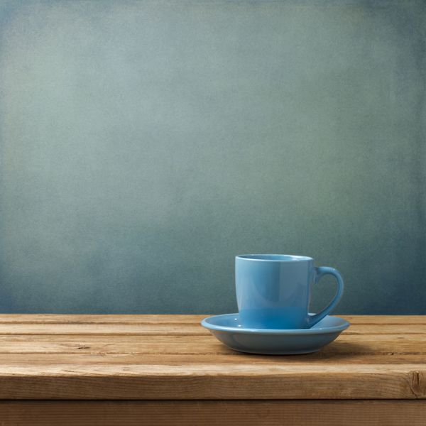 فنجان قهوه آبی روی میز چوبی روی پس زمینه آبی گرانج