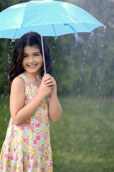 دختر جوان در حال بازی در باران با چتر